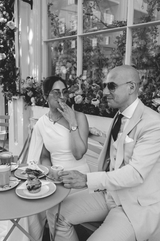 Black of white photo of Raissa and Vsileios sitting at a dainty table adorned with pastel treats. The couple savour their drinks amidst the whimsical charm of Peggy Porschen Café.
