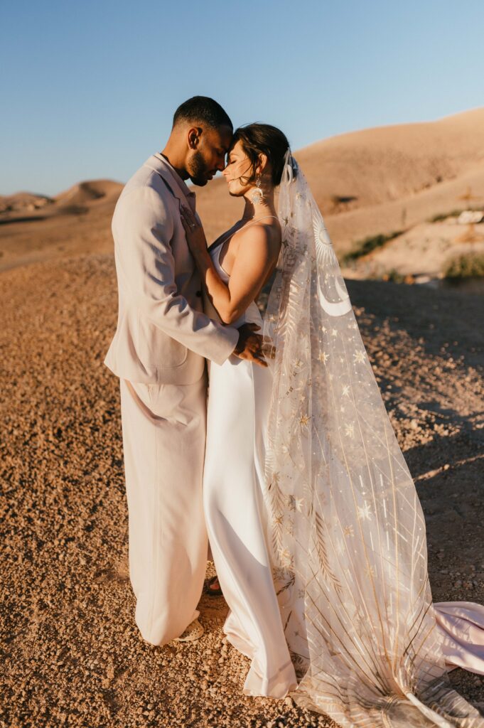 Megan and James cuddling in the soft sand of the Marrakech desert as the sun rises behind them, captured by Marrakech wedding photographer Sarah Hurja.
