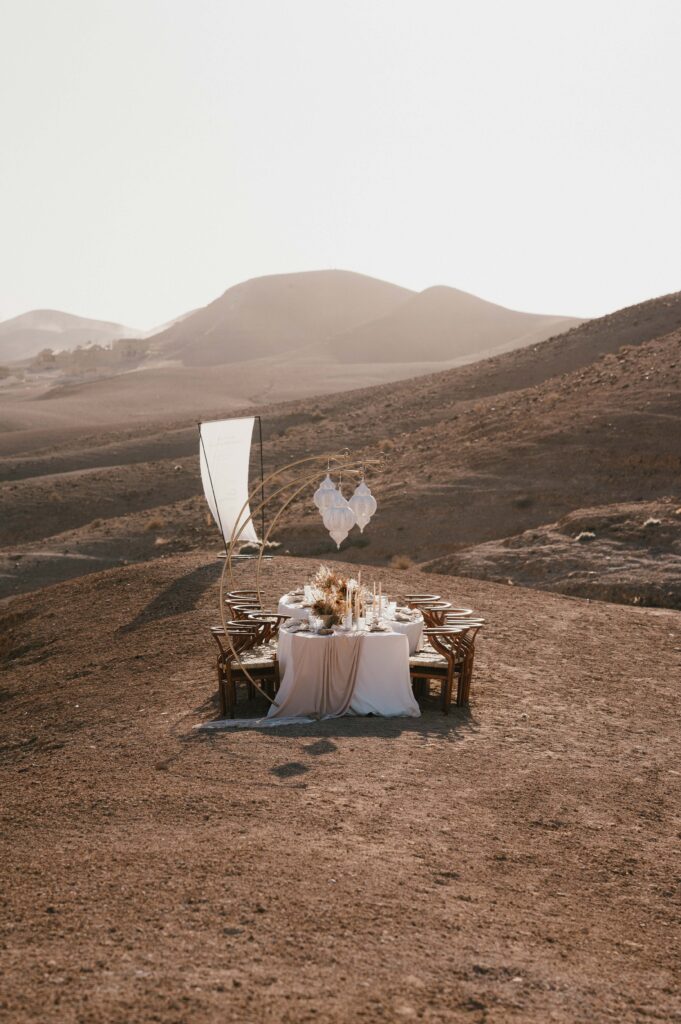 A wide shot of the intimate wedding breakfast setup on a hill overlooking Be Agafay, with the couple’s table decorated in a minimalist, boho-luxe style.