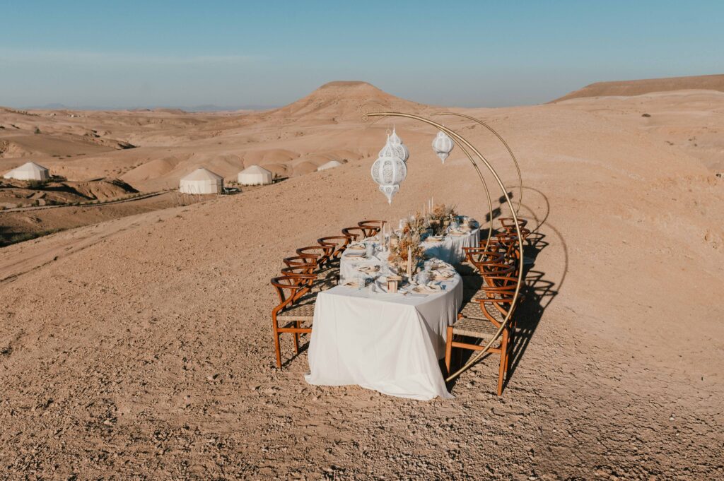 The wedding breakfast set up on a hill overlooking Be Agafay, with a "wave table" decorated with Moroccan pieces and dry florals, creating a boho-luxe vibe for the Marrakech desert elopement.