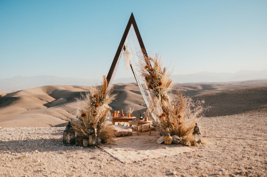 The boho-luxe ceremony setup in the sand dunes, with vibrant pillows, rustic leather seats, and twinkling fairy lights for Megan and James’ Marrakech desert elopement, designed by La Perle Events Marrakech Wedding Planner and enhanced with florals by The Bloom Room Marrakech and decor by Chabichic Morocco.