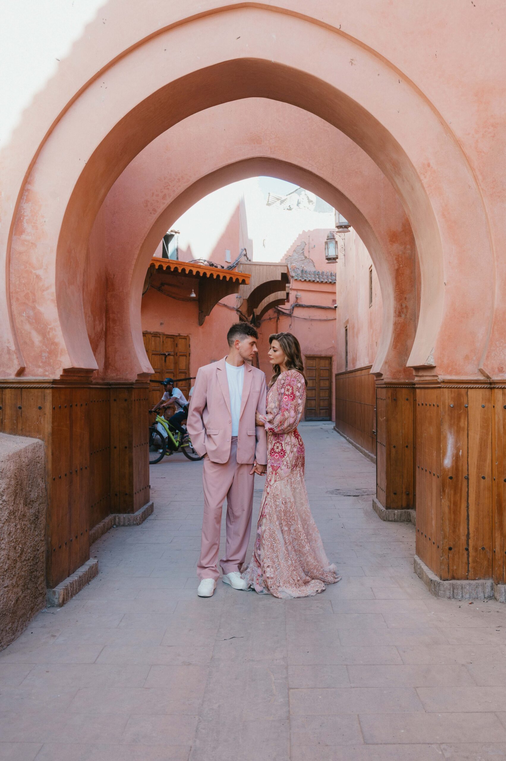 Paul and Lisa stand together in front of vibrant pink archways in the Marrakech souk, radiating love and joy on their special day.