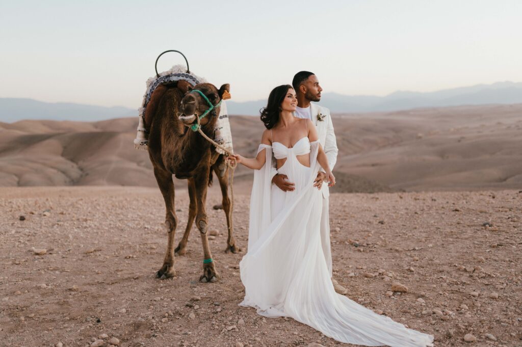 The couple, Megan and James, enjoying a tender moment on a camel ride as the sun rises over the Atlas Mountains during their Marrakech desert elopement.