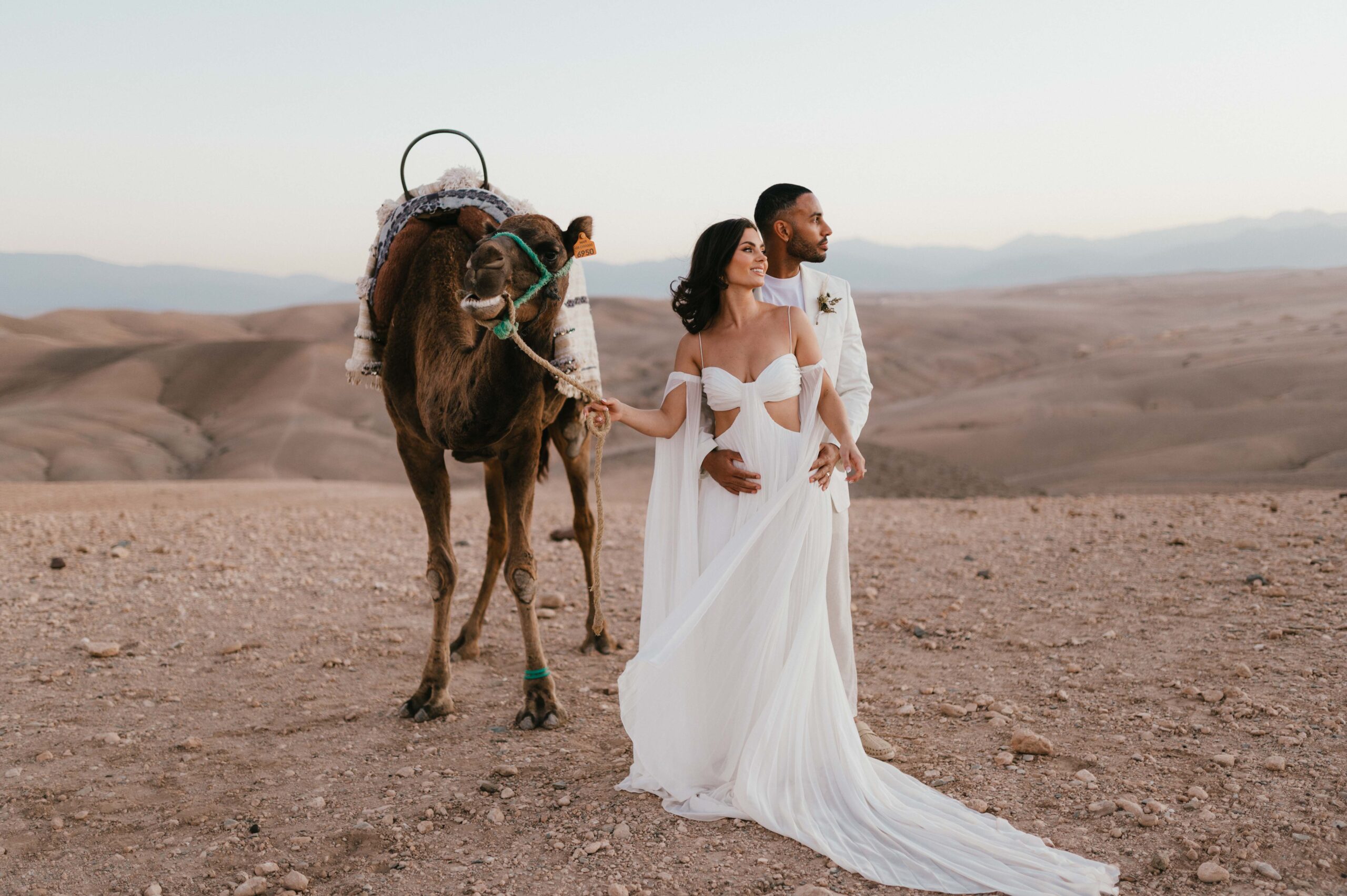 The couple, Megan and James, enjoying a tender moment on a camel ride as the sun rises over the Atlas Mountains during their Marrakech desert elopement.